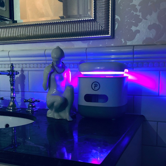 A PonicTank on a bathroom counter beside a porcelain figurine, its rim throwing magenta and blue light across the tiles.